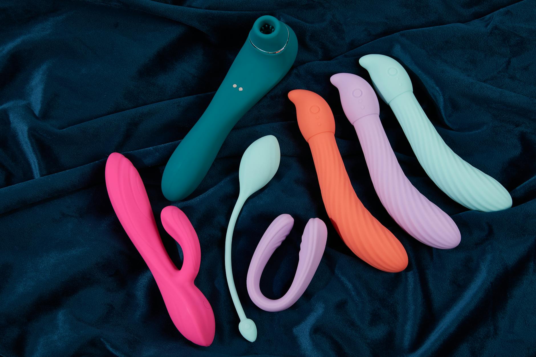 Colorful silicone vibrators and suction toys displayed on dark fabric showing design variety