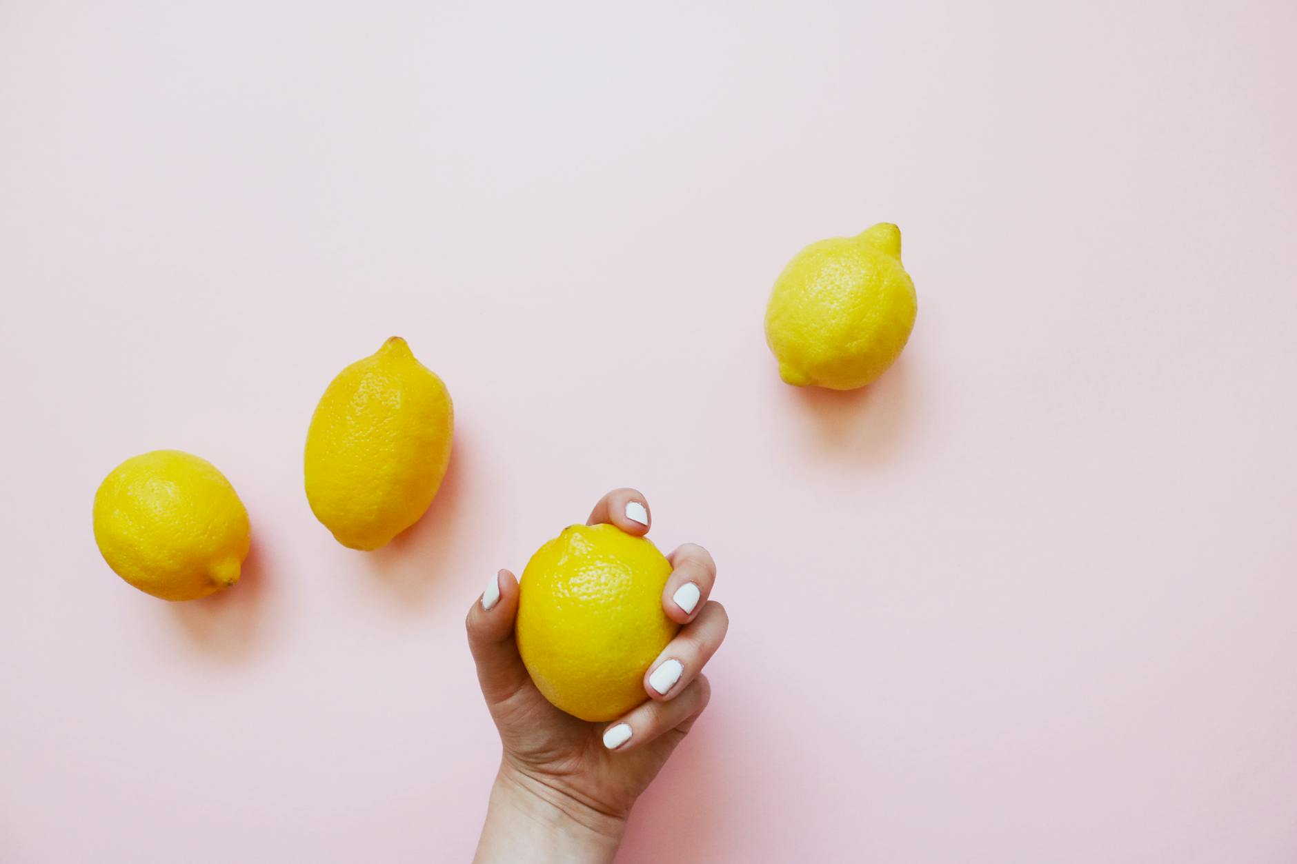 A hand holding a fresh lemon on a soft pink background, representing the careful, intentional approach to delayed arousal.