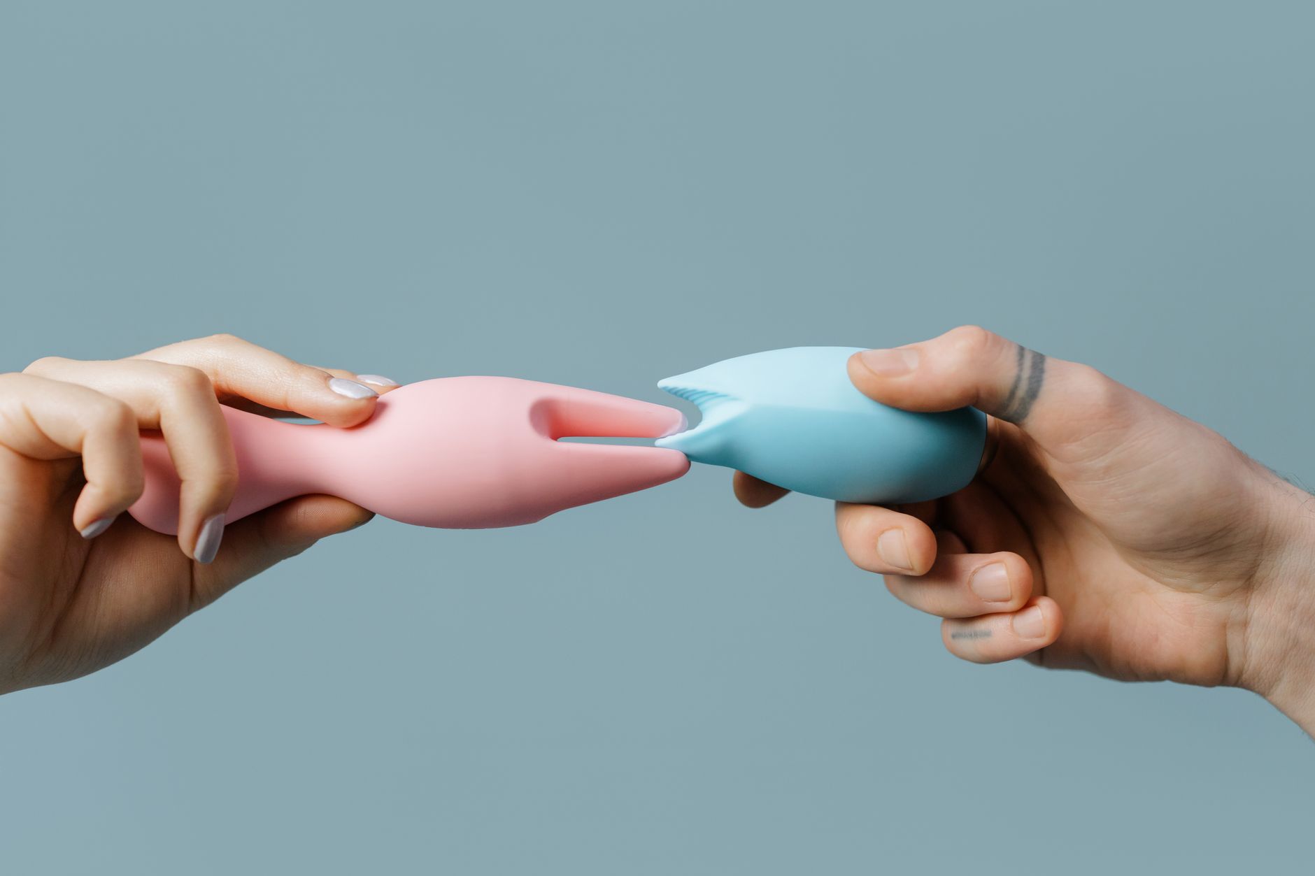 Hands holding a blue clitoral vibrator against a knitted sweater, demonstrating intimate touch and sensation.