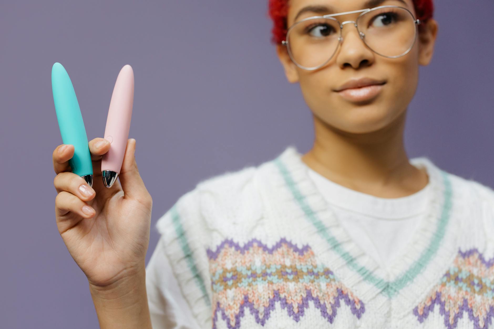 Two colorful vibrators held against a purple background, symbolizing pleasure and self-discovery